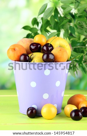 Bright summer fruits in pail on wooden table on natural background