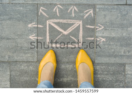 Female feet with abstract envelope message letter with arrows in different directions, written on grey sidewalk.