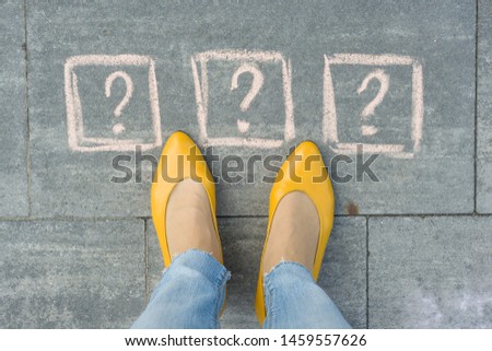 Woman feet with 3 question marks in front of her legs painted on the grey sidewalk.