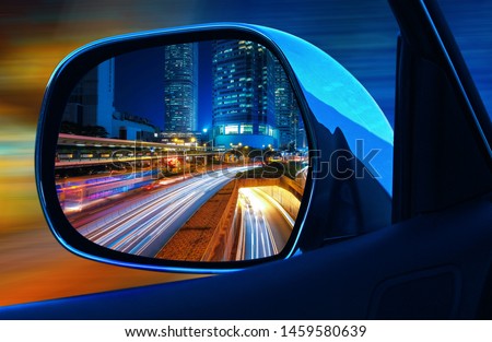 Closeup rearview mirror car at full speed at night in big modern  metropolis with skyscrapers Royalty-Free Stock Photo #1459580639