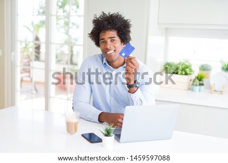 African American man using laptop and shopping online with credit card with a happy face standing and smiling with a confident smile showing teeth