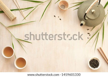 Asian food background - tea set, bowls and chopsticks with bamboo leaves on light wooden background. Asian menu design, chinese japanese cuisine concept.