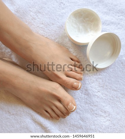 Top view photo of woman feet and toes with manicure toenails on a white towel beside skin lotion