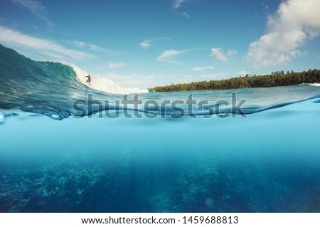 half underwater shot of surfer surfing a reef break wave in Indonesia