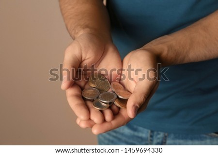 Young man with handful of coins on beige background, closeup