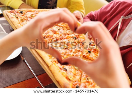 hands folded in the shape of a heart close-up on the background of fresh hot pizza Royalty-Free Stock Photo #1459701476