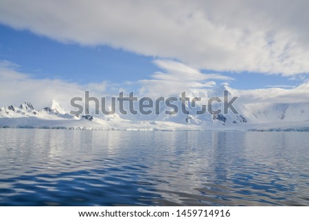 Water lay still under low hanging white clouds that cover Antarctic mountains
