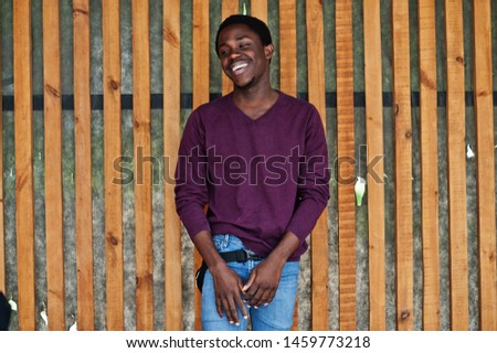 Young african american man in violet jumper posed against wooden wall.
