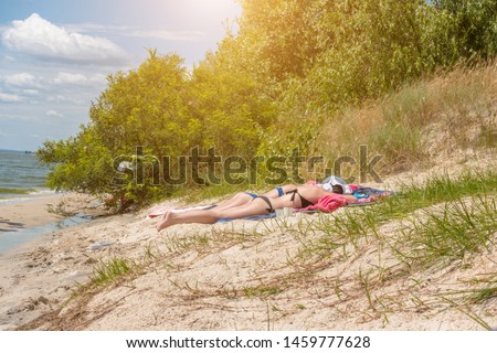 Two girls in swimsuits sunbathe on the beach by the river