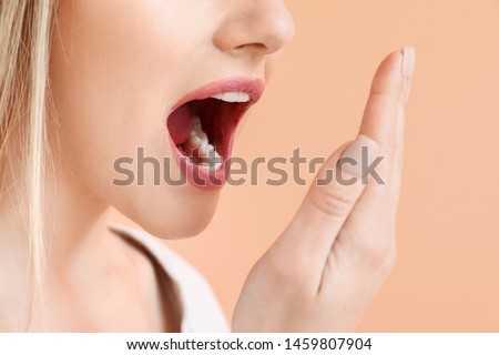 Beautiful woman checking freshness of her breath on color background, closeup