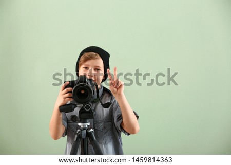 Cute little photographer with professional camera on color background