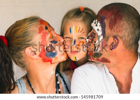 Happy family - young couple kissing baby daughter, after playing with paints.