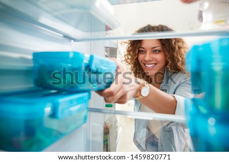 View Looking Out From Inside Of Refrigerator As Woman Takes Out Healthy Packed Lunch In Container Royalty-Free Stock Photo #1459820771