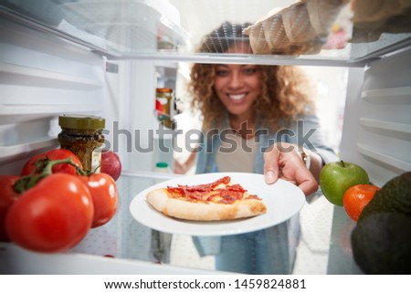 View Looking Out From Inside Of Refrigerator As Woman Opens Door For Leftover Takeaway Pizza Slice