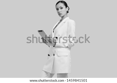 Portrait of a cute and gorgeous latin women in fashion white suit with digital tablet posing on bright studio background