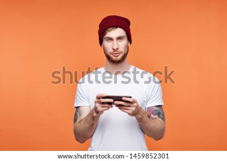 Tattoo man Red hat white T-shirt fashion style modern portrait smartphone isolated orange background lifestyle                      
