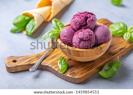 Artisanal blueberry ice cream and green basil in a wooden bowl on a serving board, selective focus.