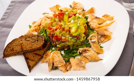 Image of  delicious salad guacamole with fresh tomatoes and arugula served with grilled trout fillet at plate