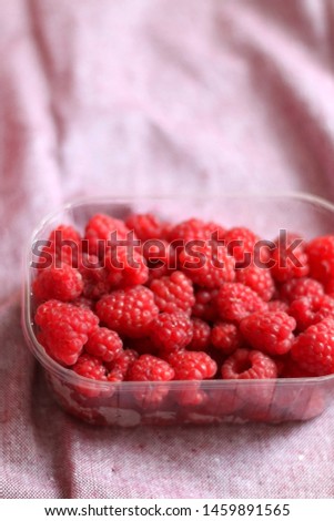Fresh raspberries in a container. Selective focus, pink background.