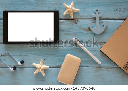 Top view of computer tablet, starfishes, pen, note book, headphones on a blue wooden background. Copy space.