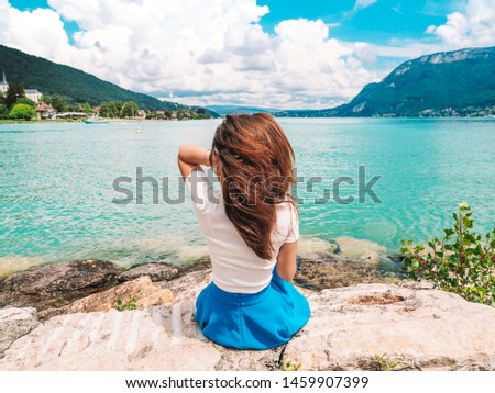 Brunette girl with long hair in a blue skirt posing against the background of a Beautiful view of the lake in Annecy in France, clear azure water, yachts and the Alps