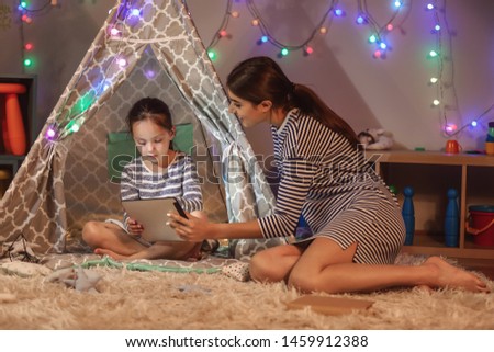 Mother and her little daughter with tablet computer at home in evening