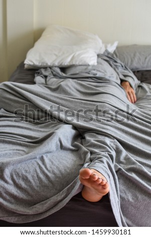 man laying in bed under a gray sheet with a white pillow on his head to block out the light