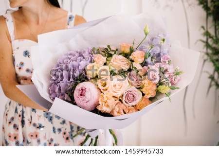 Very nice young woman holding big and beautiful bouquet of fresh hydrangea, peony, roses, eustoma, carnations in peach and lavender colors, cropped photo, bouquet close up