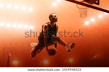 Athletic african american basketball player scoring a layup basket during a professional basketball game. Red floodlit background