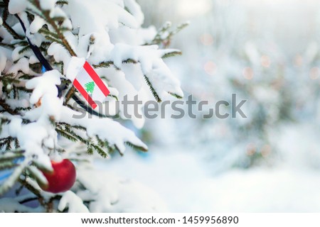 Christmas Lebanon. Xmas tree covered with snow, decorations and a flag of Lebanon. Snowy forest background in winter. Christmas greeting card.