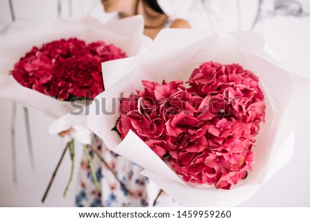 Very nice young woman holding two big and beautiful bouquets of fresh vivid pink hydrangea flowers wrapped in white paper, cropped photo, bouquet close up