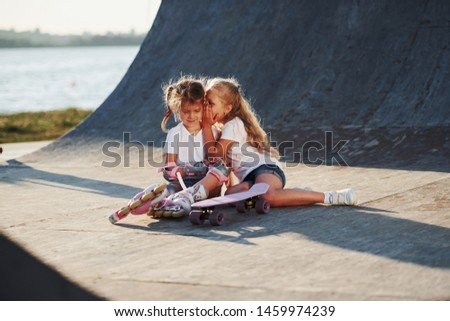 Relaxing and have conversation. On the ramp for extreme sports. Two little girls with roller skates outdoors have fun.