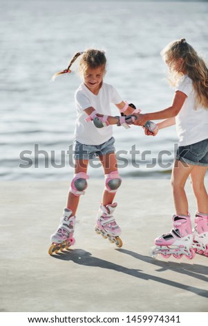 Two kids learning how to ride on roller skates at daytime near the lake.