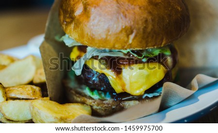 Fresh, tasty, juicy hamburger with cheese, tomatoes, seasoned marbled beef, fresh salad and potatoes on a wooden table. Side view. Close-up