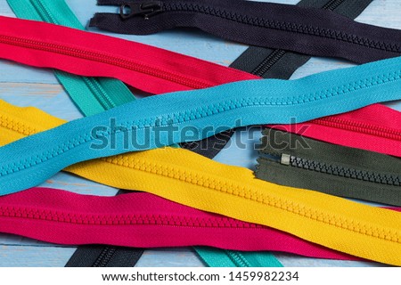 Pack a lot of colorful plastic zippers stripes with sliders pattern for handmade sewing tailoring on the blue denim background close up selective focus