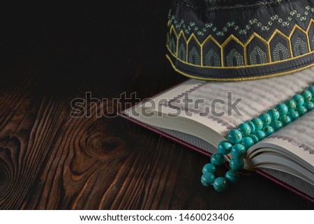 Islamic book Koran with rosary beads and pray hat for muslims on grey background