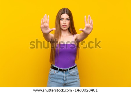 Young woman over isolated yellow background making stop gesture and disappointed