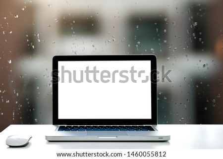 Workspace white desk with blank screen laptop for your photomontage or product display and wireless mouse,Raindrops on window with blurred out background. - Image