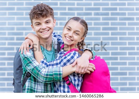 Two happy schoolchildren with backpacks against a brick wall outdoors. Cute children - pupils teen girl hugs boy. Back to school. Concepts of friends, childhood, first love and education.