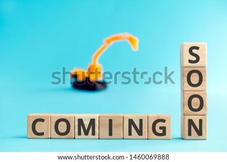 coming soon wooden cubes letters yellow toy excavator, development page under construction or technical work concept blue background