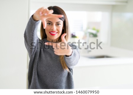 Young beautiful woman wearing winter sweater at home smiling making frame with hands and fingers with happy face. Creativity and photography concept.