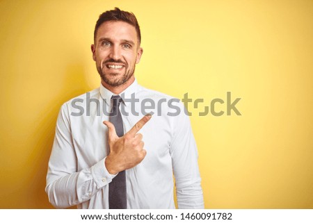 Young handsome business man wearing elegant white shirt over yellow isolated background cheerful with a smile of face pointing with hand and finger up to the side with happy and natural expression 