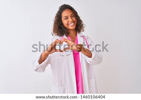 Young brazilian doctor woman wearing stethoscope standing over isolated white background smiling in love showing heart symbol and shape with hands. Romantic concept.
