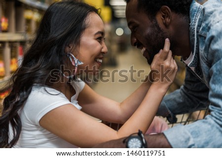 selective focus of happy asian girl touching face of handsome and cheerful african american man 