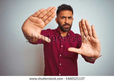 Young indian man wearing red elegant shirt standing over isolated grey background doing frame using hands palms and fingers, camera perspective