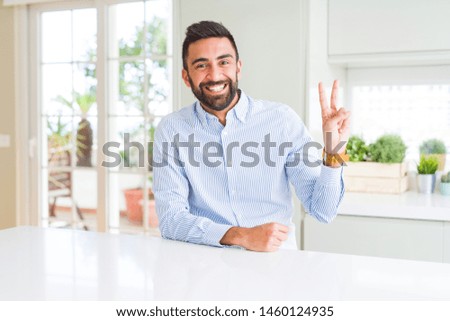 Handsome hispanic business man smiling with happy face winking at the camera doing victory sign. Number two.