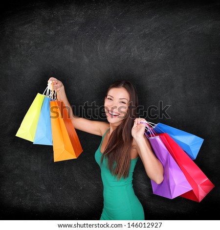 Shopping woman holding shopping bags on blackboard background with copy space for your text or design. Happy excited female shopper showing purchases excited and joyful. Mixed race Asian girl