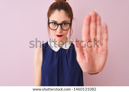 Redhead woman with pigtail wearing elegant dress and glasses over isolated pink background doing stop sing with palm of the hand. Warning expression with negative and serious gesture on the face.