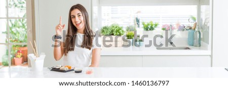 Wide angle picture of beautiful young woman eating asian sushi from delivery pointing finger up with successful idea. Exited and happy. Number one.