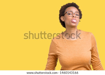 Young beautiful african american woman wearing glasses over isolated background sticking tongue out happy with funny expression. Emotion concept.